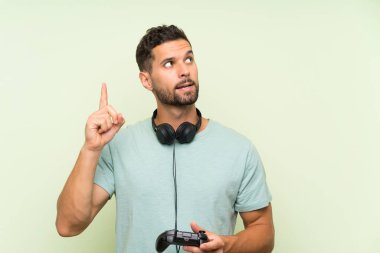 Genç yakışıklı adam izole yeşil duvar üzerinde bir video oyunu denetleyicisi ile oynarken bir parmak kaldırırken çözüm gerçekleştirmek niyetinde