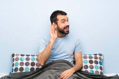 Yatakta bir şey dinleyen adam, elini kulağına koyar.