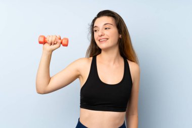 Ağırlık kaldıran genç sporcu kadın izole edilmiş mavi arka planda mutlu bir ifadeyle.