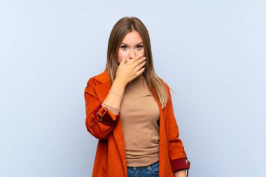İzole edilmiş mavi arka planı olan genç kız elleriyle ağzını kapatıyor.