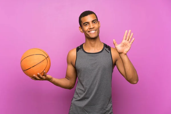 Jovem Desportista Com Bola Basquete Sobre Parede Roxa Isolada Saudando — Fotografia de Stock