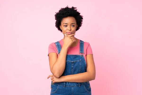 在孤立的粉色背景下穿着工作服的非洲裔美国女人在想办法 — 图库照片