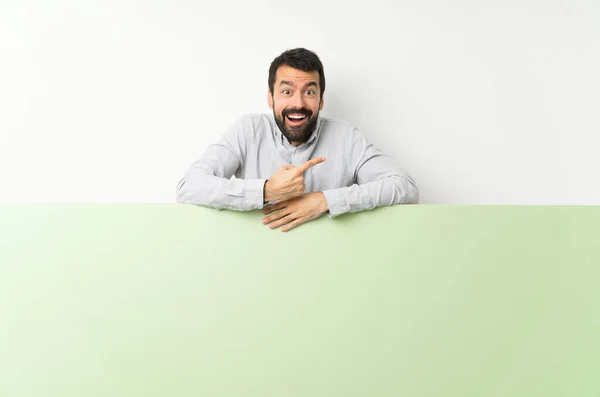 Young Handsome Man Beard Holding Big Green Empty Placard Surprised — Stock Photo, Image