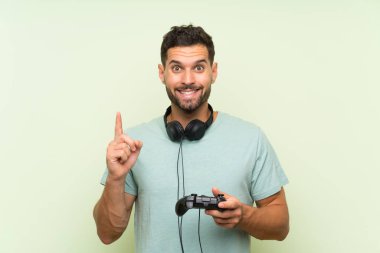 Genç yakışıklı adam izole yeşil duvar üzerinde bir video oyunu denetleyicisi ile oynayan harika bir fikir işaret