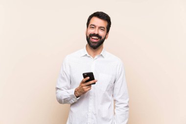 Sakallı genç adam elinde cep telefonuyla gülüyor.