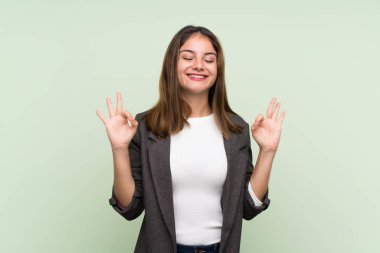 Zen pozisyonunda, yeşil arka planda ceketi olan esmer genç bir kız.