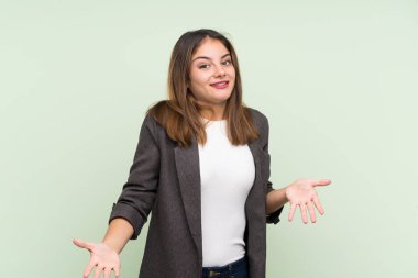 Ceketli, yeşil arka planda sırıtan esmer genç kız.