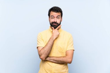 Sakallı genç adam soyutlanmış mavi arka planda düşünüyor.