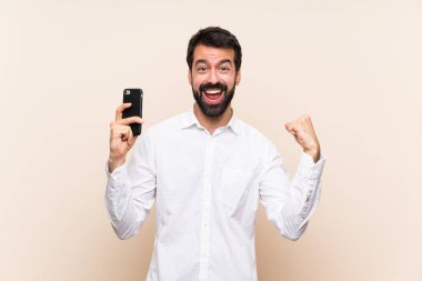 Elinde cep telefonu olan sakallı genç adam şaşırdı ve bir mesaj gönderiyor.