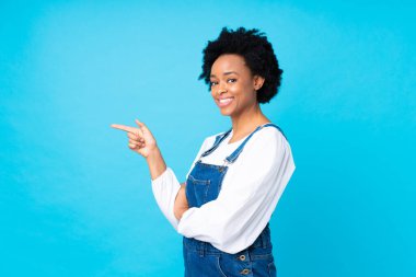 İşçi tulumu giymiş, mavi arka planı olan Afro-Amerikalı bir kadın.