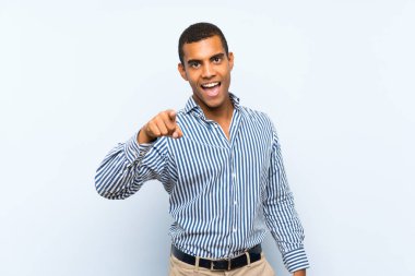 Genç, yakışıklı, esmer, soyutlanmış, mavi arka planda, şaşırmış ve ön tarafı işaret eden adam.