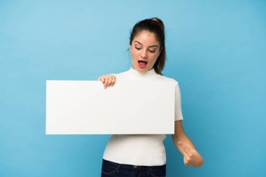 Genç esmer kız izole edilmiş mavi arka planda boş beyaz bir levha tutuyor.