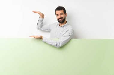 Sakallı genç yakışıklı bir adam büyük yeşil boş bir afiş tutuyor.