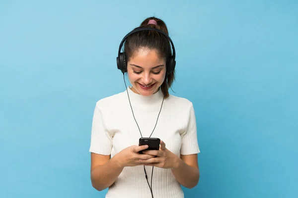 Jovem Morena Sobre Fundo Azul Isolado Usando Celular Com Fones — Fotografia de Stock