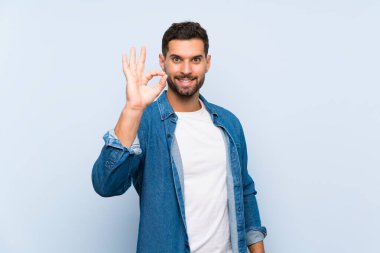 İzole edilmiş mavi arkaplanda yakışıklı bir adam parmaklarıyla tamam işareti gösteriyor
