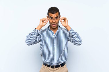 Genç, yakışıklı, esmer, soyutlanmış, mavi arka planlı, gözlüklü ve şaşırmış bir adam.