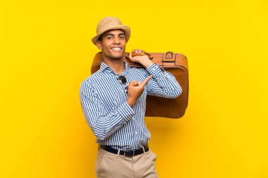 Esmer adam izole sarı arka plan üzerinde bir ürün sunmak için yan işaret bir vintage evrak çantası tutan