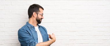 Beyaz tuğla duvarın üstünde sakallı yakışıklı bir adam.