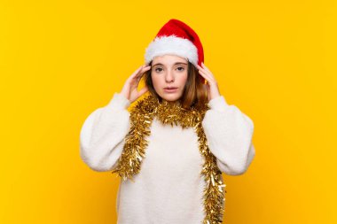 İzole edilmiş sarı arka planda Noel şapkası takan bir kız mutsuz ve hayal kırıklığına uğramış. Olumsuz yüz ifadesi