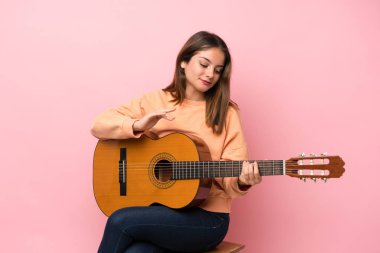 İzole edilmiş pembe arka planda gitar çalan esmer bir kız.
