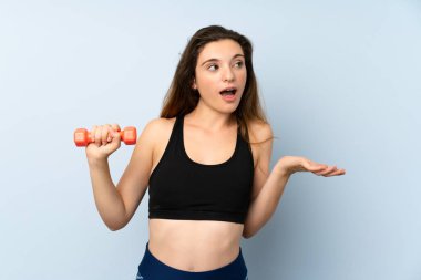 Ağırlık kaldıran genç bir bayan, yalıtılmış mavi arka planda, sürpriz bir yüz ifadesi var.