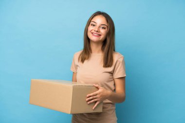 Genç esmer kız izole edilmiş mavi arka planda bir kutu tutuyor ve başka bir yere götürüyor.