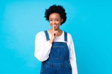 Tulumuyla izole edilmiş mavi arka planı olan Afro-Amerikalı kadın sessizlik hareketi yapıyor.