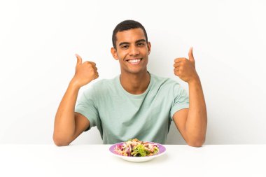 Bir masada salata ile genç yakışıklı adam jest kadar bir başparmak veren