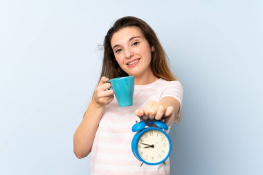 Genç esmer kız bir fincan kahve ve klasik saati izole edilmiş arka planda tutuyor.
