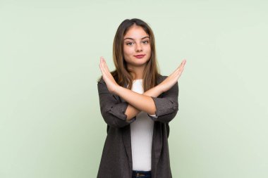 Yeşil arka planda ceketi olan esmer genç kız jest yapmıyor.