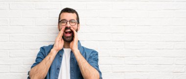 Beyaz tuğla duvarın üzerinde sakallı yakışıklı bir adam bağırıyor ve bir şeyler söylüyor.