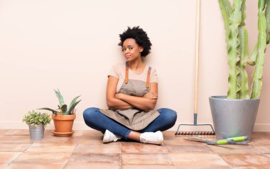 Bahçıvan kadın kolları bağlı yerde oturuyor ve ileriye bakıyor.