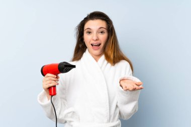 Yüzünde şok ifadesi olan saç kurutma makinesi olan bornozlu genç bir kadın.