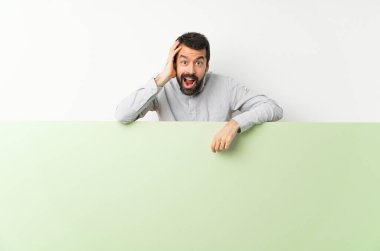 Sakallı genç yakışıklı adam elinde kocaman boş bir pankart tutuyor.