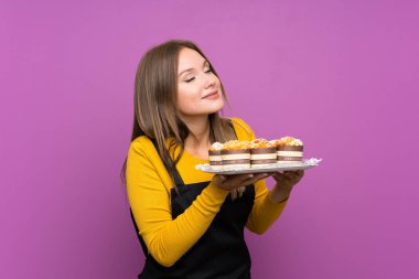 Genç kız izole mor arka plan üzerinde farklı mini kek çok tutan