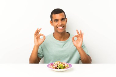 Parmakları ile ok işareti gösteren bir masada salata ile genç yakışıklı adam