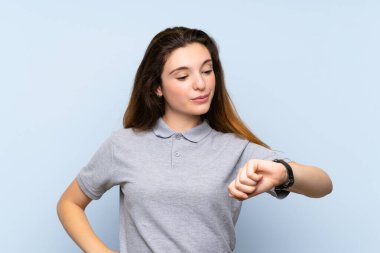 Kol saatine bakarak izole edilmiş mavi arka planda esmer bir kız.