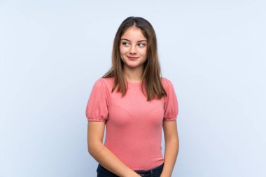 Genç esmer kız, izole edilmiş mavi arka planda duruyor ve yan tarafa bakıyor.