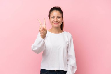 Pembe arka planda genç esmer kız gülümsüyor ve zafer işareti gösteriyor.