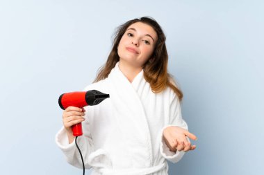 Bornozlu, saç kurutma makinesi olan genç bir kadın omuzlarını kaldırırken şüpheyle hareket ediyor.