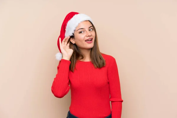 Jong Meisje Met Kerst Hoed Geïsoleerde Achtergrond Luisteren Iets — Stockfoto