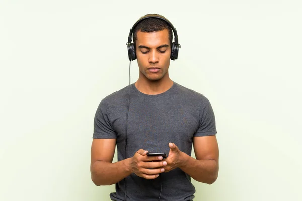 Junger gutaussehender Mann hört Musik mit Handy über isolierte grüne Mauer — Stockfoto