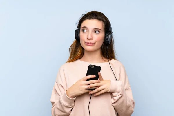 Young Brunette Girl Isolated Blue Background Using Mobile Headphones Thinking — Stock Photo, Image