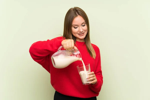 Chica adolescente sosteniendo un vaso de leche sobre un fondo verde aislado — Foto de Stock