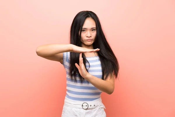 年轻的亚洲女孩在孤立的粉红背景上做着时间的手势 — 图库照片