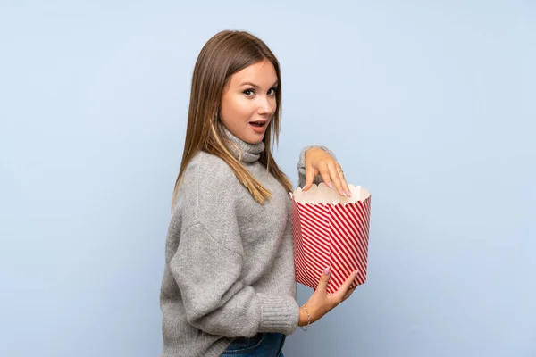 ティーン女の子とともにセーター以上隔離された青背景食べるポップコーン — ストック写真