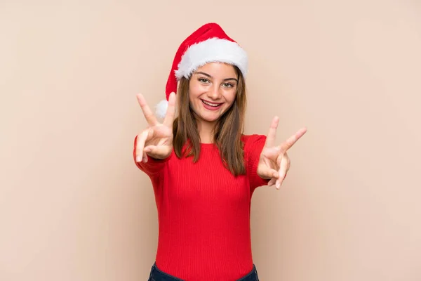 年轻姑娘头戴圣诞礼帽 背景孤寂 面带微笑 显露出胜利的迹象 — 图库照片