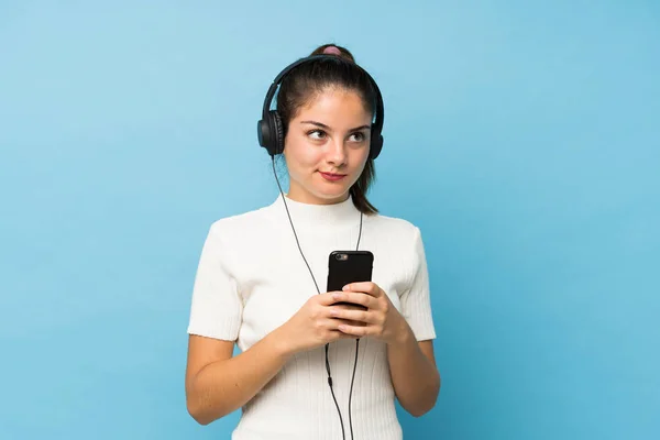 Mladá Brunetka Dívka Přes Izolované Modré Pozadí Pomocí Mobilu Sluchátky — Stock fotografie