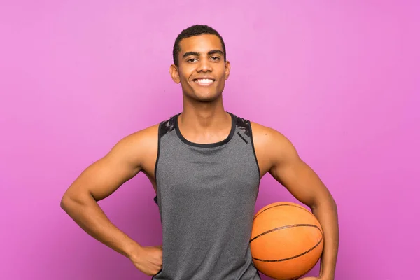 Jovem desportista com bola de basquete sobre parede roxa isolada — Fotografia de Stock