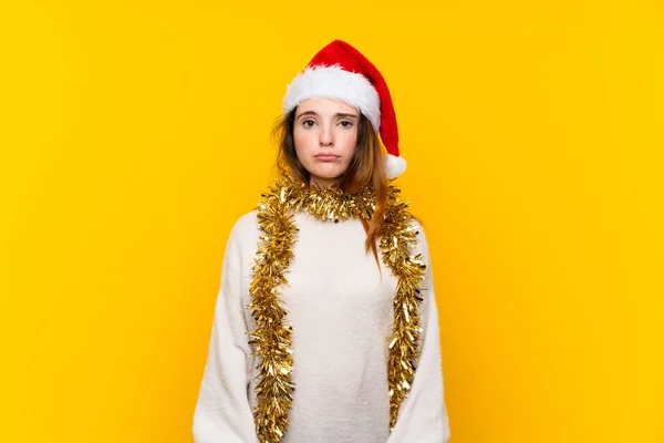Girl with christmas hat over isolated yellow background sad